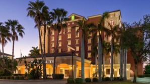 Een hotel met een rode gevel, meerdere verdiepingen en palmbomen op de voorgrond.