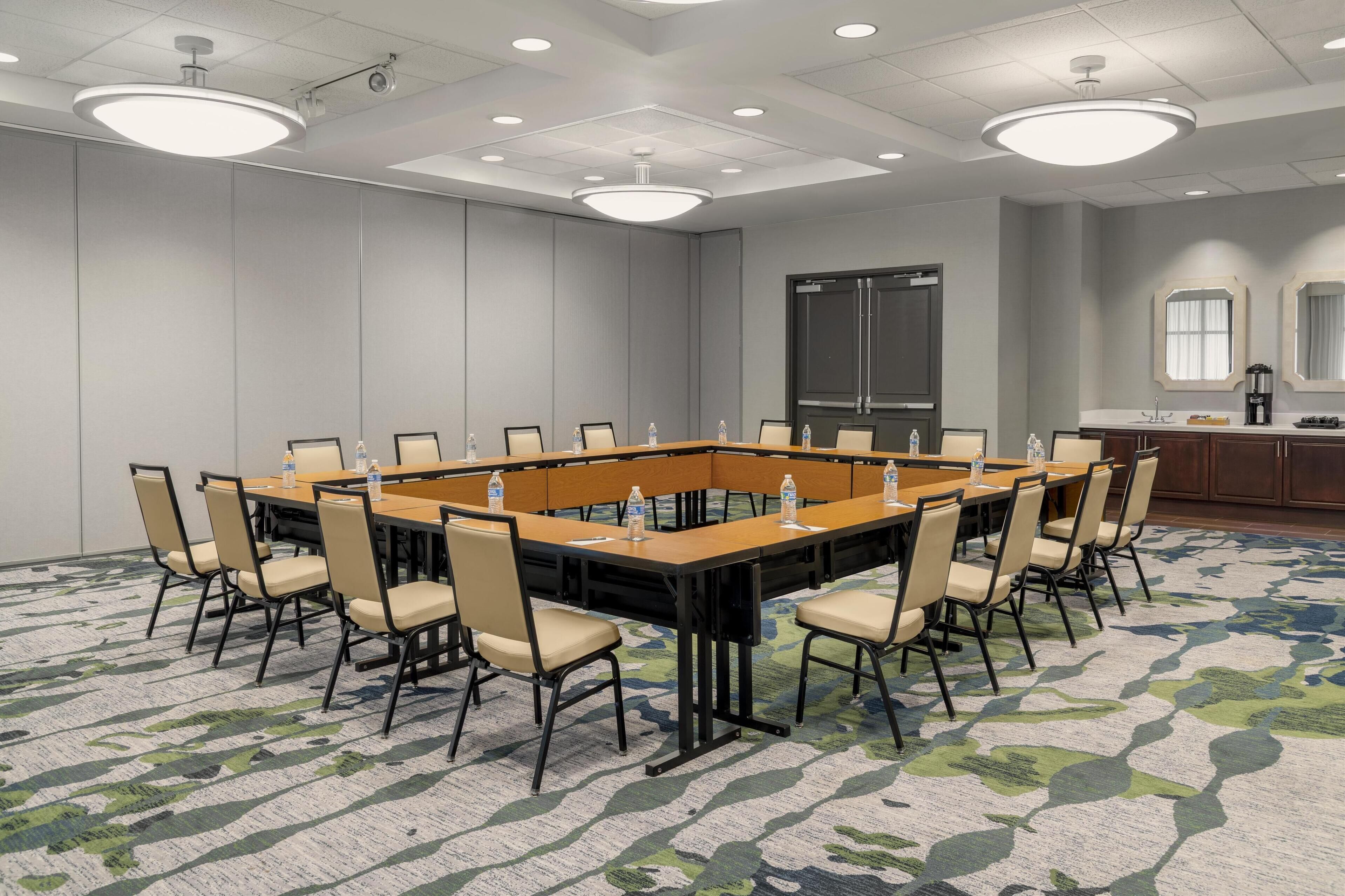 Een vergaderzaal met een lange rechthoekige tafel, meerdere stoelen en een vloerbedekking.
