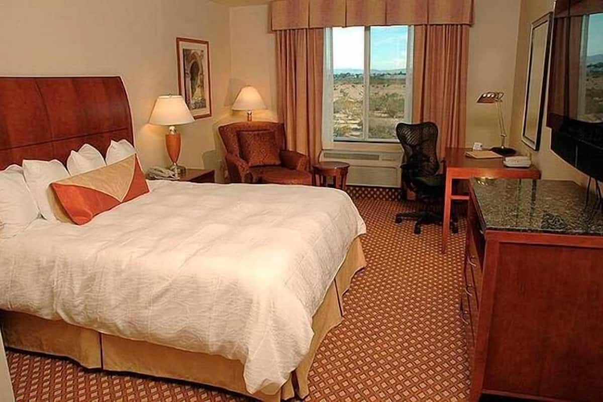 Une chambre d’hôtel avec un grand lit, deux fauteuils, un bureau, une télévision et une fenêtre donnant sur un beau paysage.