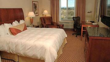 A hotel room with a large bed, a desk, a chair, and a television.