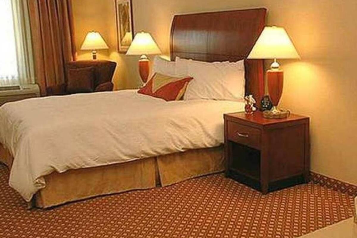 Une chambre d’hôtel avec un lit, deux tables de chevet avec des lampes, une petite table et un tapis à motifs.