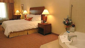 Et hotelværelse med en stor seng, to sengeborde med lamper, et badeværelse med badekar og en vase med blomster.