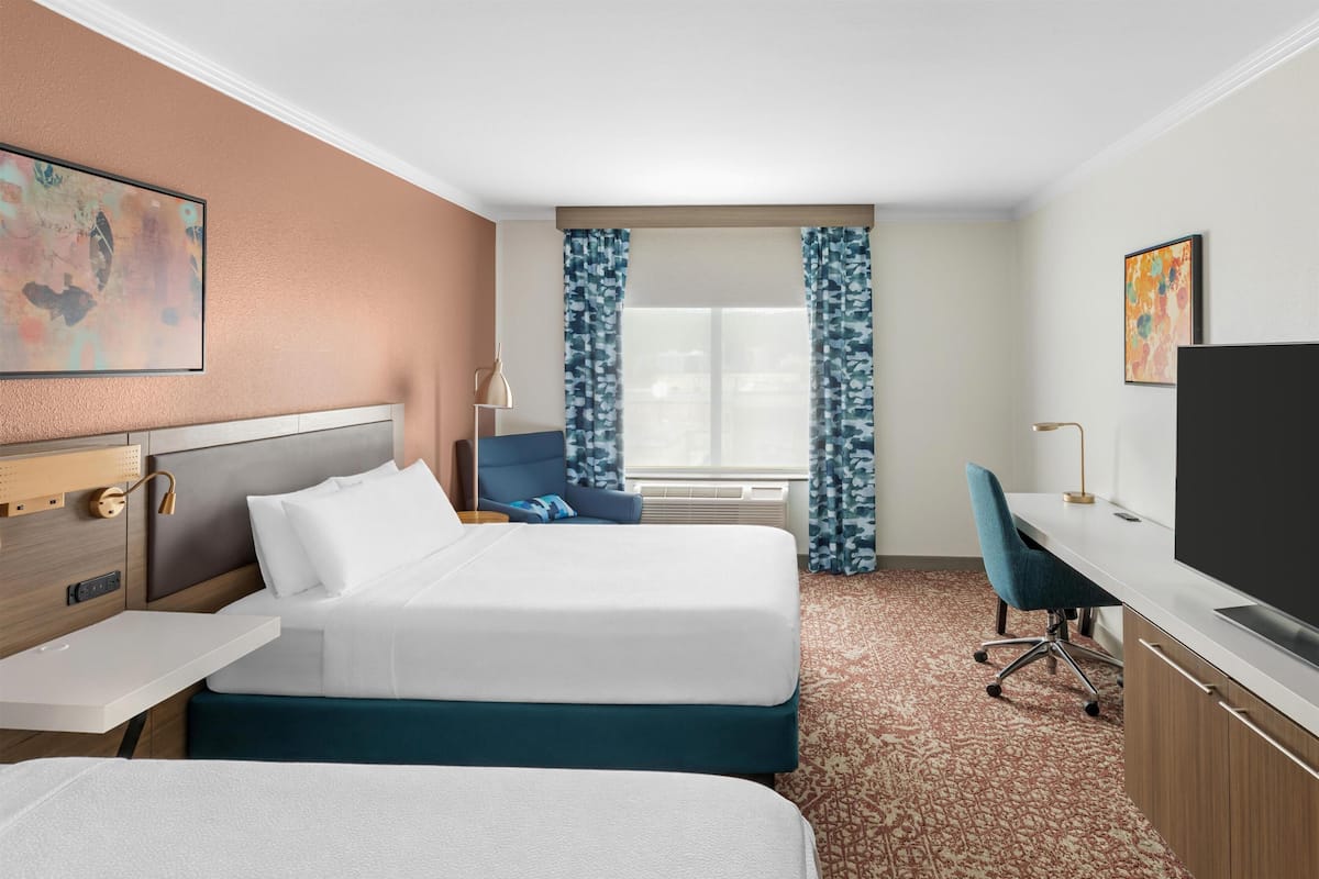 A hotel room with two beds, a desk, a chair, a television, and a window with curtains.