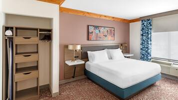 A hotel room with a bed, a wardrobe, a nightstand, a lamp, a painting, and a window with curtains.