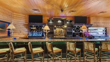 Un bar con paredes y techo de madera, que cuenta con una barra, taburetes y una pantalla de televisión.