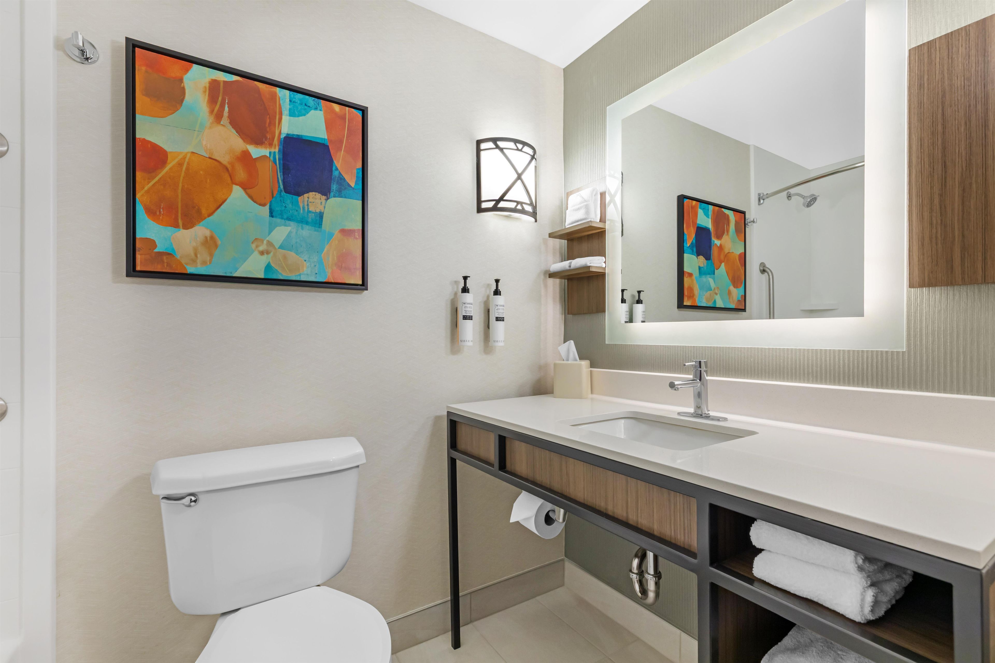 A modern bathroom with a toilet, sink, mirror, and abstract art.