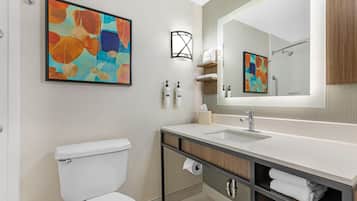 Une salle de bain moderne équipée de toilettes, d’un lavabo, d’un miroir et d’une œuvre d’art abstraite.