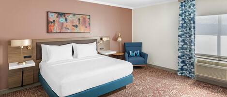 A hotel room with a bed, a chair, a nightstand, a lamp, a painting, and a window with curtains.