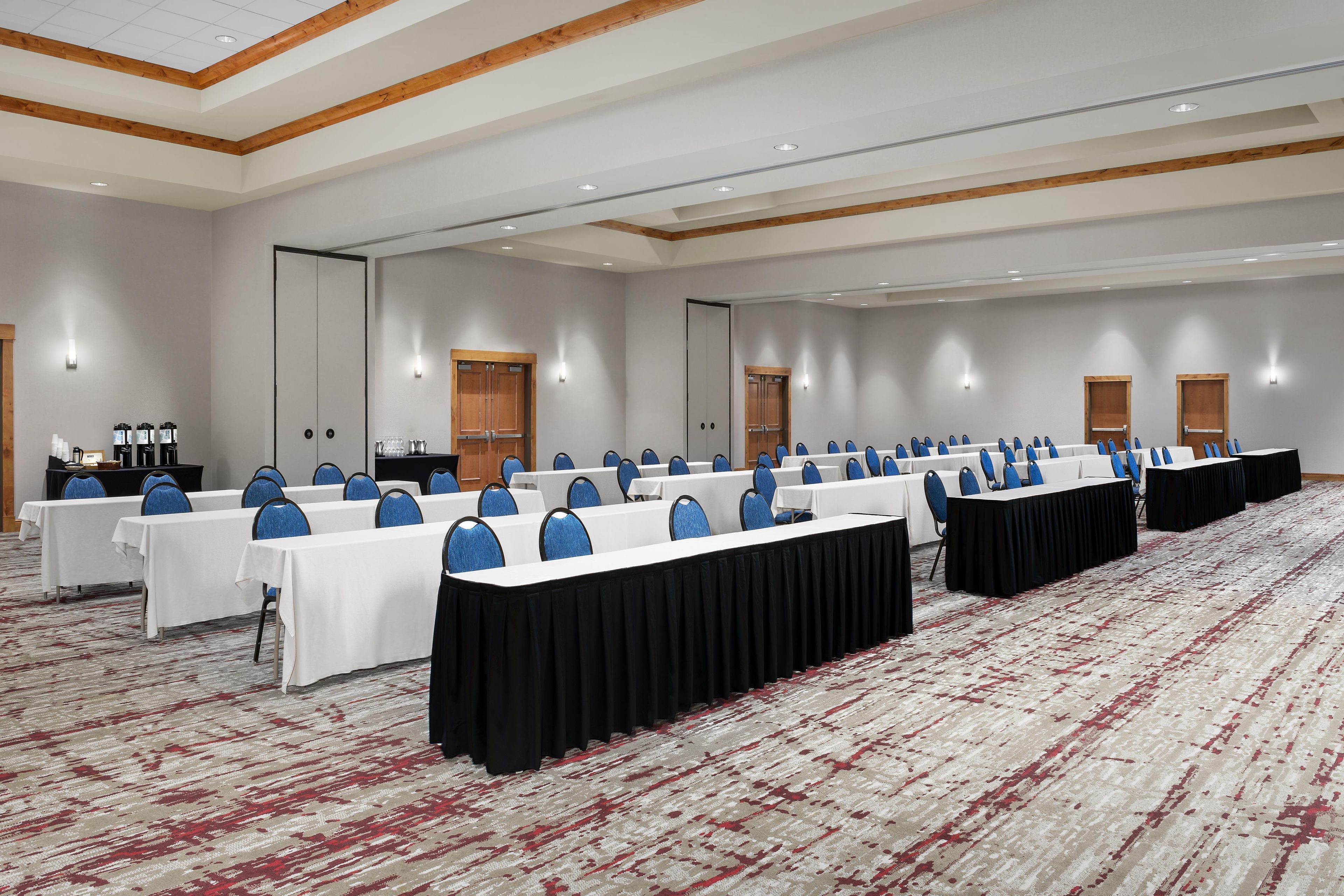 Un salón de conferencias con varias mesas, sillas y piso alfombrado.
