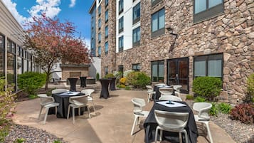 An outdoor patio with tables and chairs, a stone building, and a clear sky.