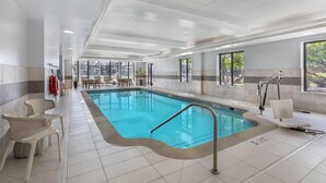 Ein Hallenbad mit klarem Wasser, umgeben von gefliestem Boden, Korbstühlen und einem Rettungsschwimmerstand.