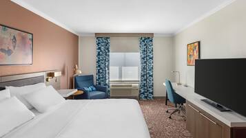 Habitación de hotel con cama, escritorio, silla, televisor y ventana con cortinas.
