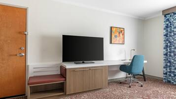 Une chambre d’hôtel avec un bureau en bois, une télévision, une chaise, un banc, un tableau et un tapis à motifs.