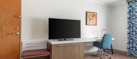 Une chambre d’hôtel avec un bureau en bois, une télévision, une chaise, un banc, un tableau et un tapis à motifs.