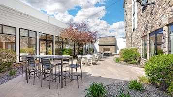 An outdoor patio area with tables and chairs, surrounded by stone walls and vegetation.