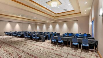 A conference room with rows of tables and chairs, a patterned carpet, and a wooden ceiling with recessed lighting.
