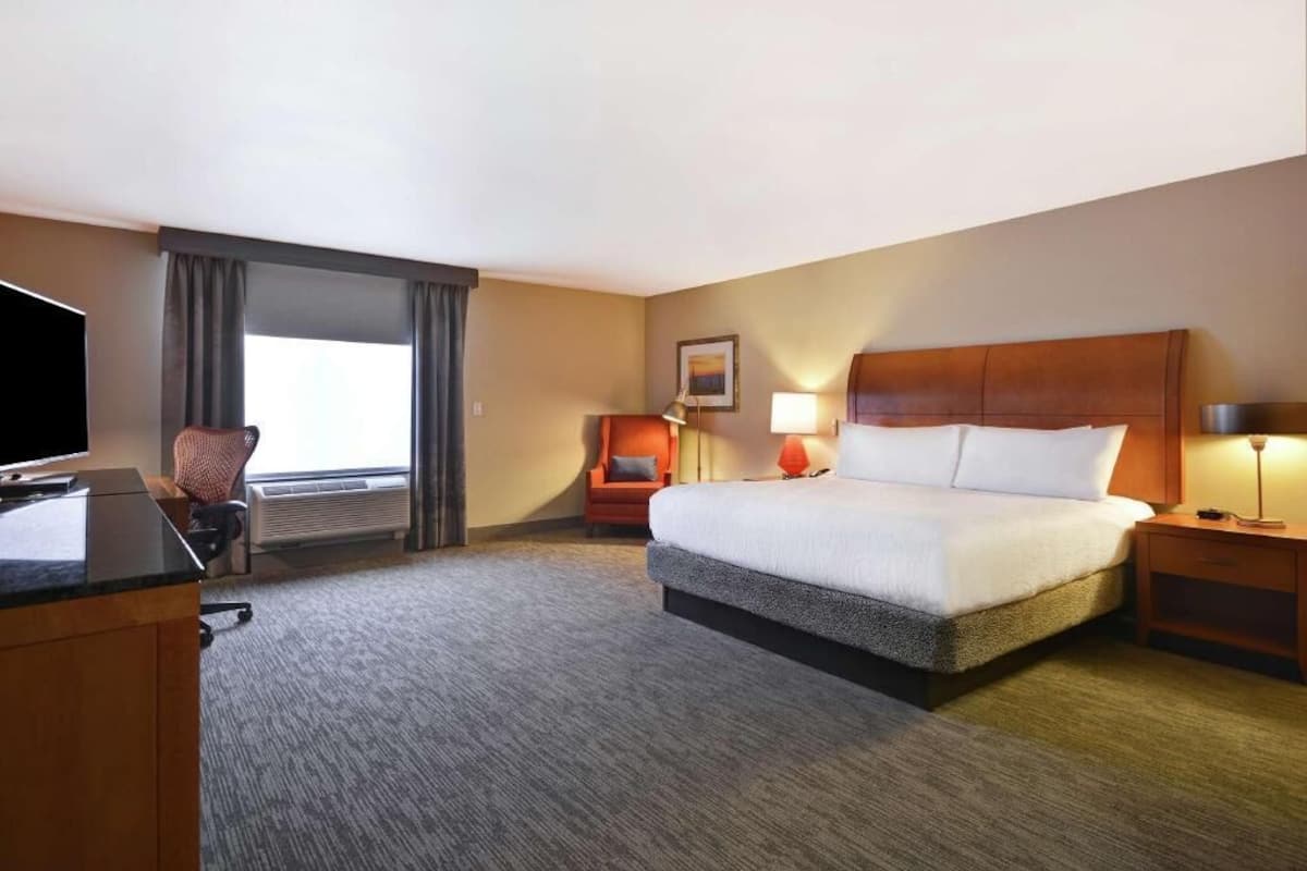 A hotel room with a bed, a desk, a chair, a TV, a lamp, and a window with curtains.