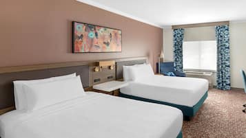 A hotel room with two beds, a painting on the wall, a desk, a chair, and a window with curtains.
