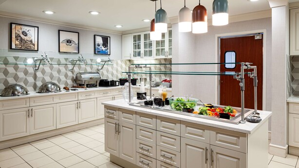 Una cocina moderna con armarios blancos, una isla central con barra para ensaladas e iluminación colgante.