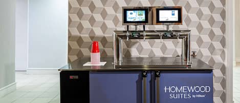 A self-service beverage station with two monitors, a coffee machine, and a water dispenser.