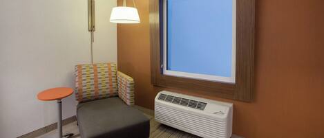 A small hotel room with a single bed, a bedside table, a chair, a window, and a wall-mounted air conditioner.