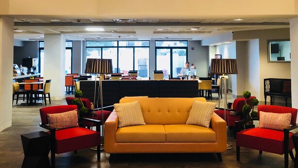 Eine geräumige Lobby mit einer zentralen Couch, roten Sesseln und einer hohen Decke mit einem Balkon.