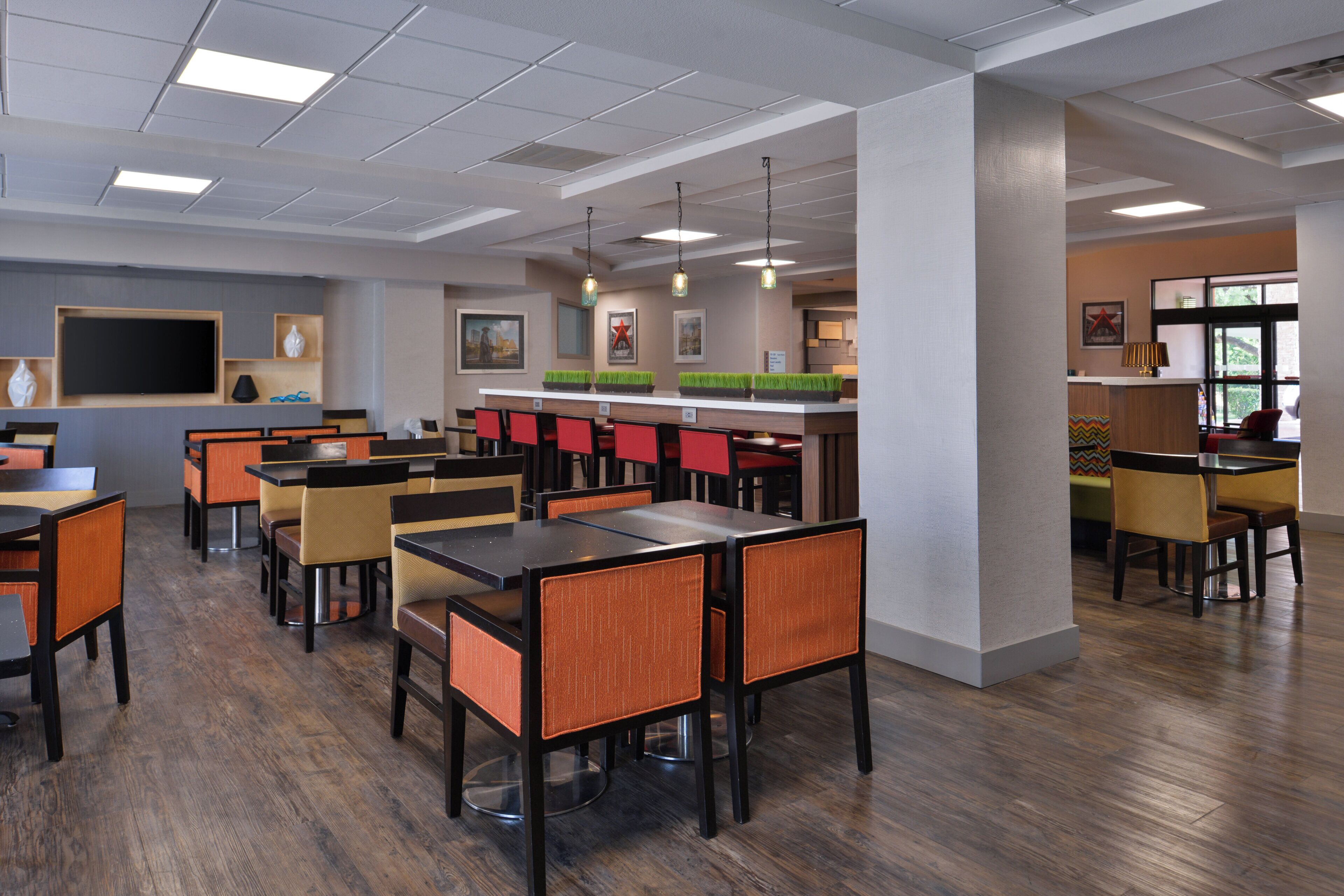 A modern dining area with multiple tables and chairs, a bar counter, and a flat-screen TV mounted on the wall.