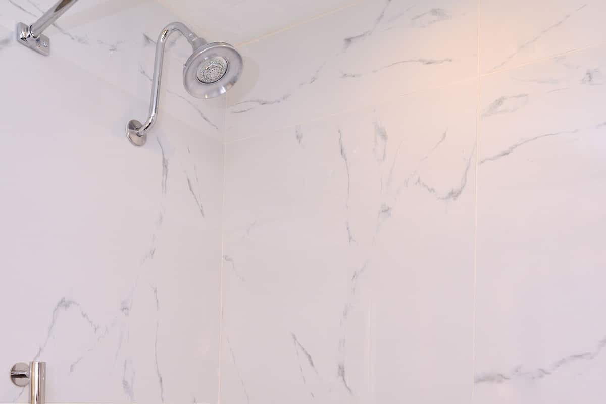 Ein Badezimmer mit weißen Marmorfliesen, einer Badewanne, einer Dusche inklusive Handbrause und einer Haltestange.