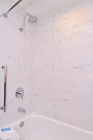A bathroom with white marble tiles, a bathtub, a shower with a handheld showerhead, and a grab bar. - Holiday Inn Express & Suites Austin North Central by IHG (Austin)