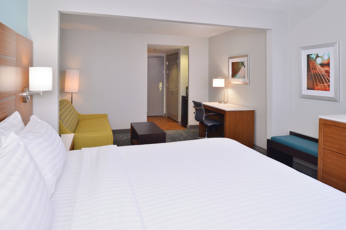 Ett hotellrum med en säng, ett skrivbord, en stol, ett litet bord och en soffa.