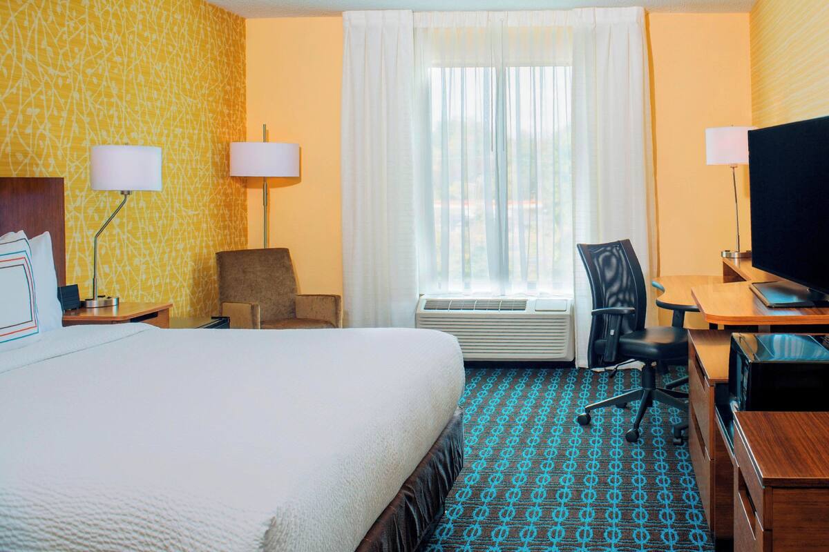 A hotel room with a large bed, a desk with a computer, a chair, and a television.
