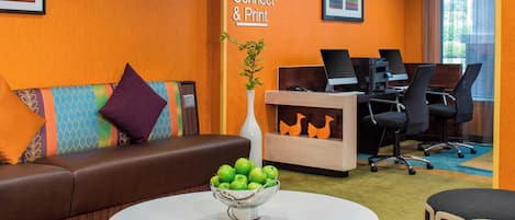 A modern office space with a brown leather sofa, a white table with a bowl of green apples, and a desk with computers.