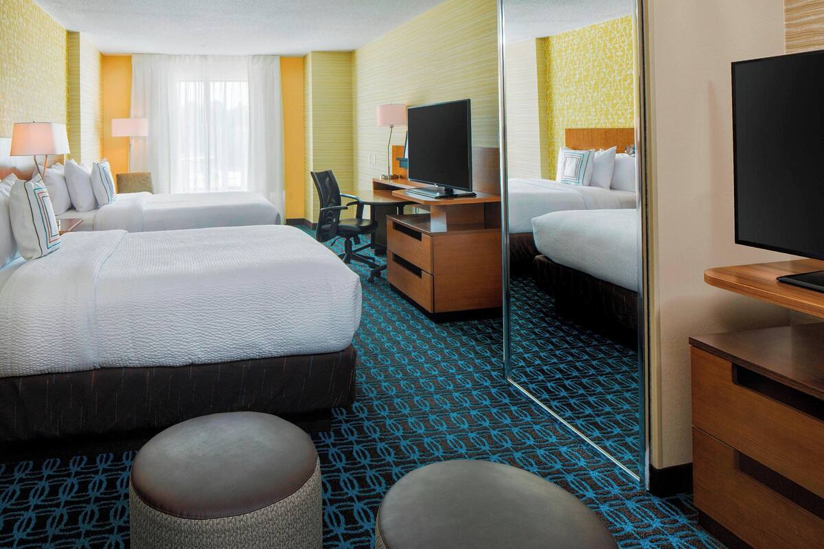 A hotel room with two beds, a desk with a computer, a TV, and a mirror.