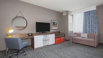 A hotel room with a desk, chair, television, sofa, and a large window with curtains.