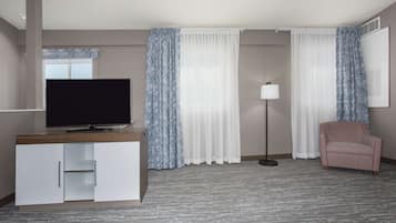 A hotel room with a flat-screen TV, a sofa, a lamp, and a large window with sheer curtains.