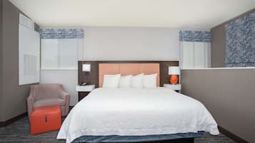 A hotel room with a large bed, a chair, a nightstand, and a window with patterned curtains.