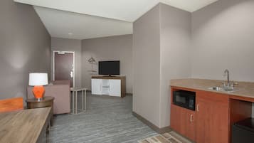 A compact hotel room with a kitchenette, a dining area, and a television.