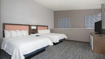 Ein Hotelzimmer mit zwei Betten, einem Schreibtisch, einem Fernseher und einem Fenster mit gemusterten Vorhängen.