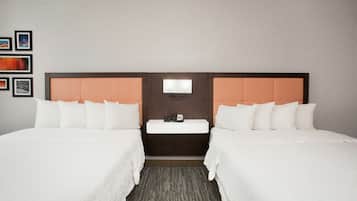 A hotel room with two beds, a nightstand with a lamp, and a wall-mounted TV.