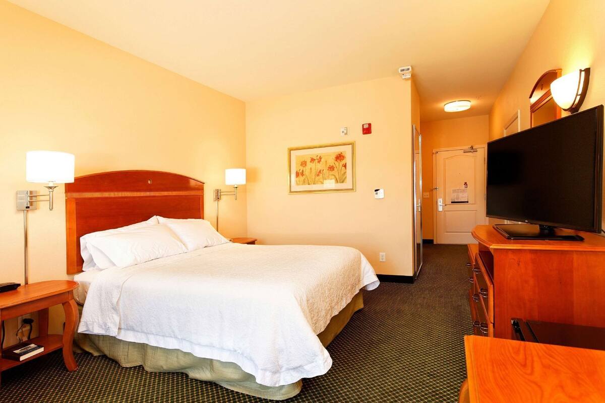 A hotel room with a bed, bedside lamps, a television, a desk, and a door leading to a bathroom.