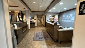 Un espace d’accueil d’hôtel comprenant un comptoir de réception, un panneau d’accueil et un espace d’attente avec une horloge.