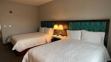 Habitación de hotel con dos camas, una mesita de noche con lámpara y cabecero con detalle en color aguamarina.