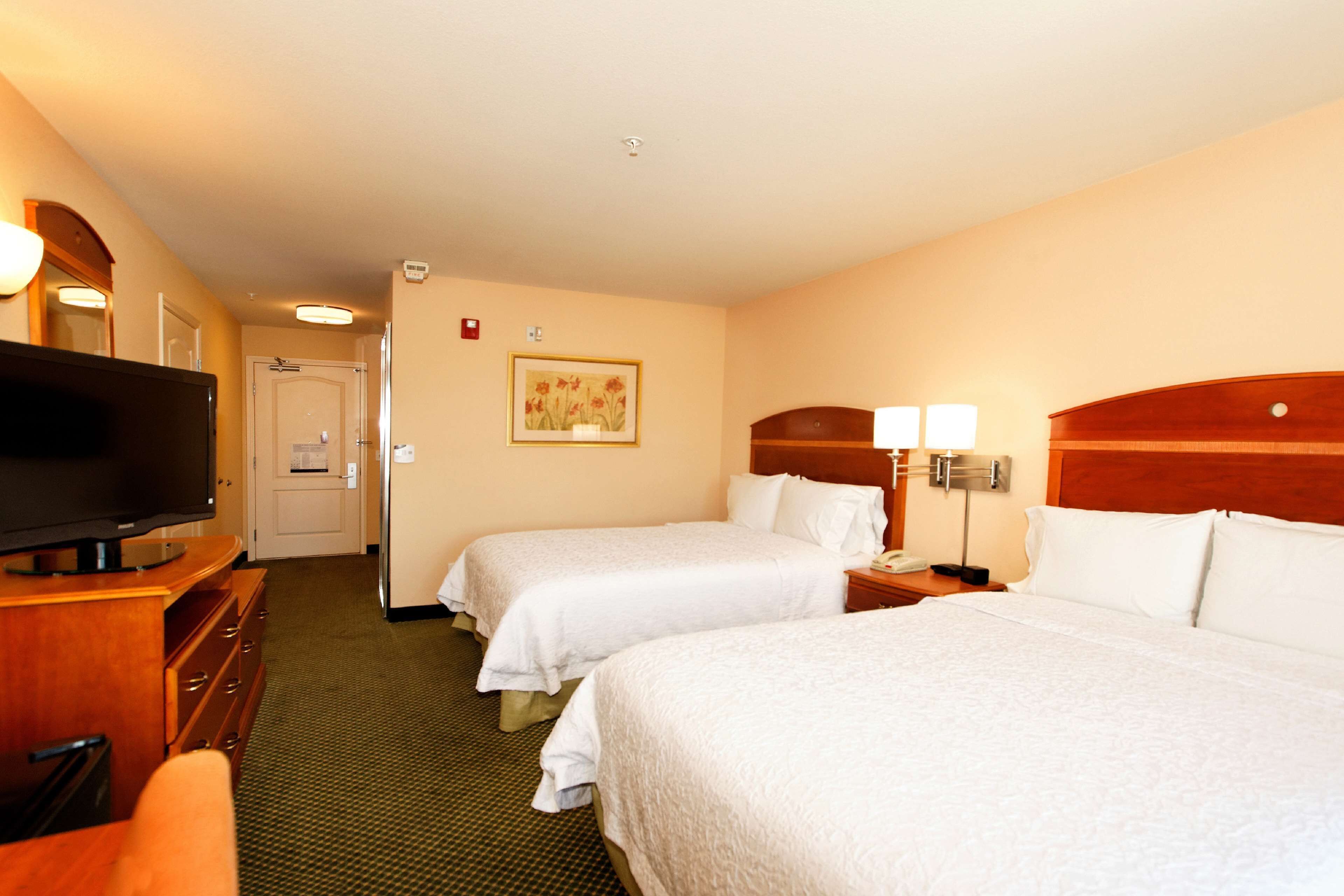 A hotel room with two beds, a TV, a desk, and a painting on the wall.