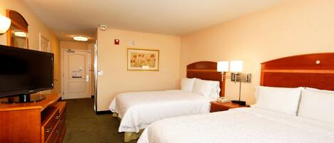A hotel room with two beds, a TV, a desk, and a painting on the wall.