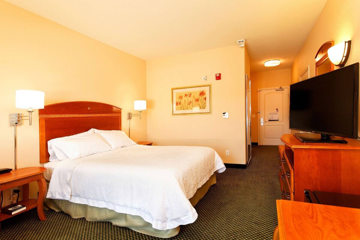 A hotel room with a large bed, bedside tables, a television, and a painting on the wall.