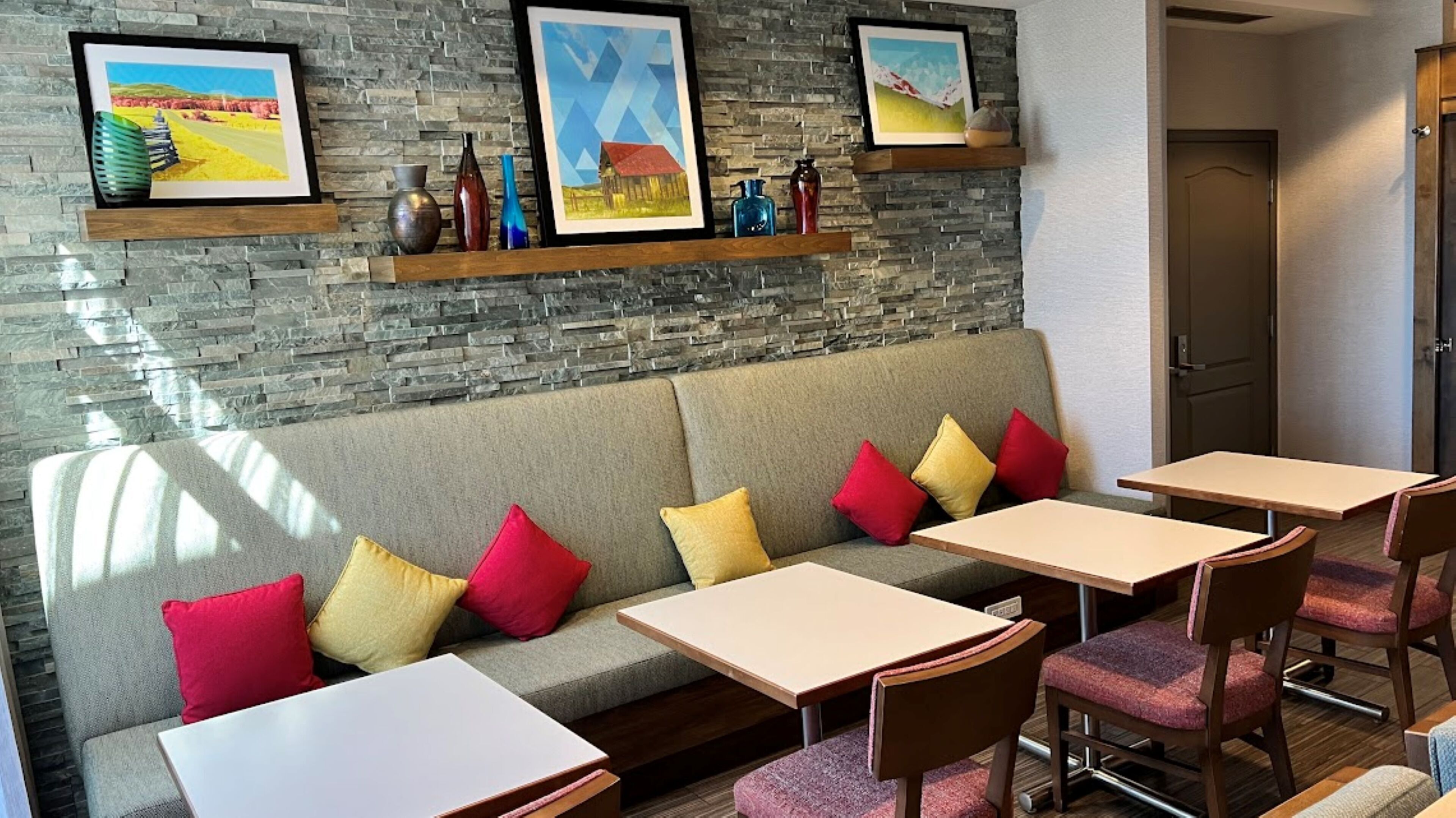 A modern lounge area with a stone wall, a sofa with colorful cushions, and a dining setup with tables and chairs.