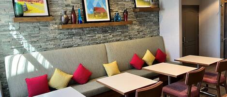 A modern lounge area with a stone wall, a sofa with colorful cushions, and a dining setup with tables and chairs.