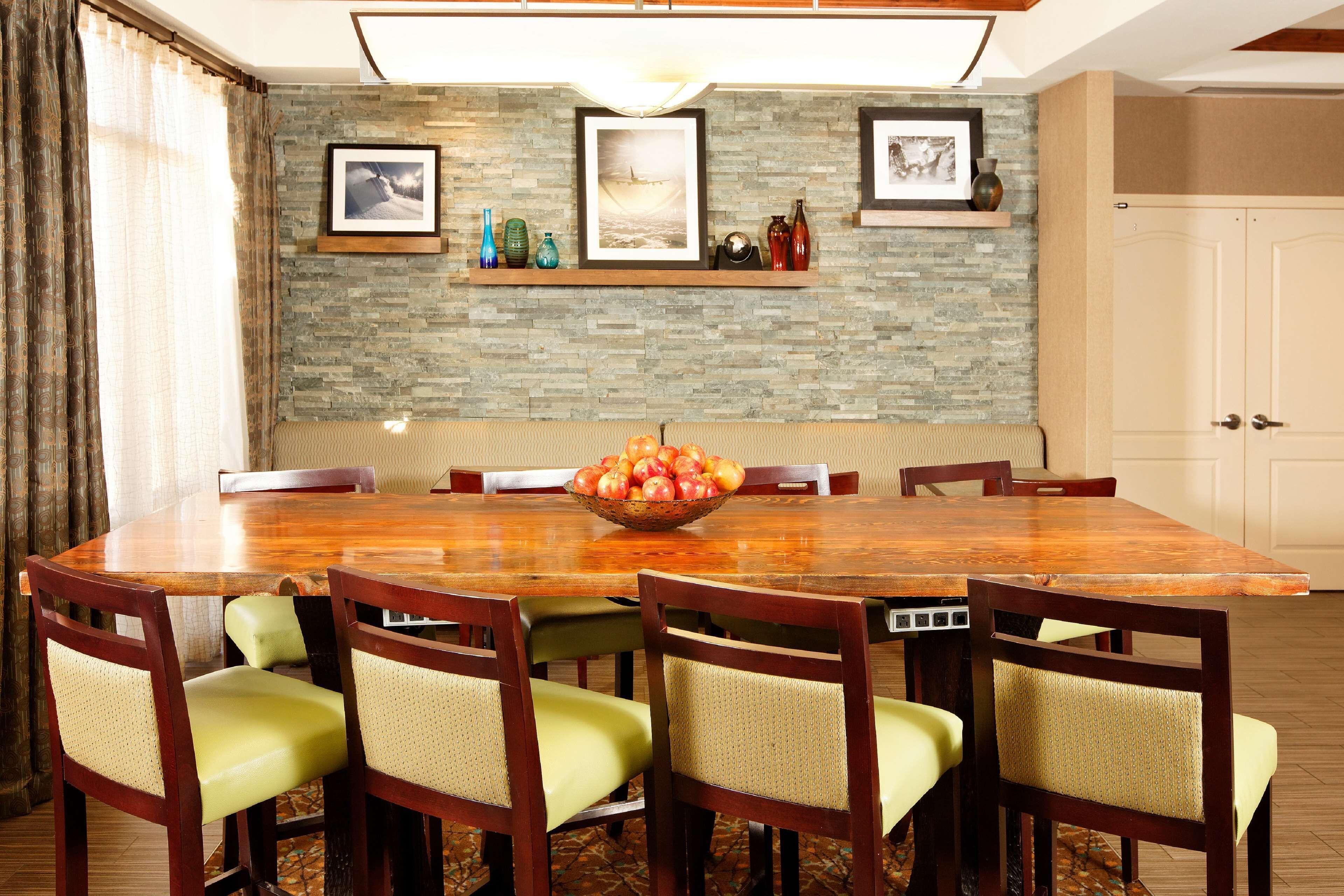 A dining room with a wooden table, six chairs, a fruit bowl, a stone wall, and framed pictures.