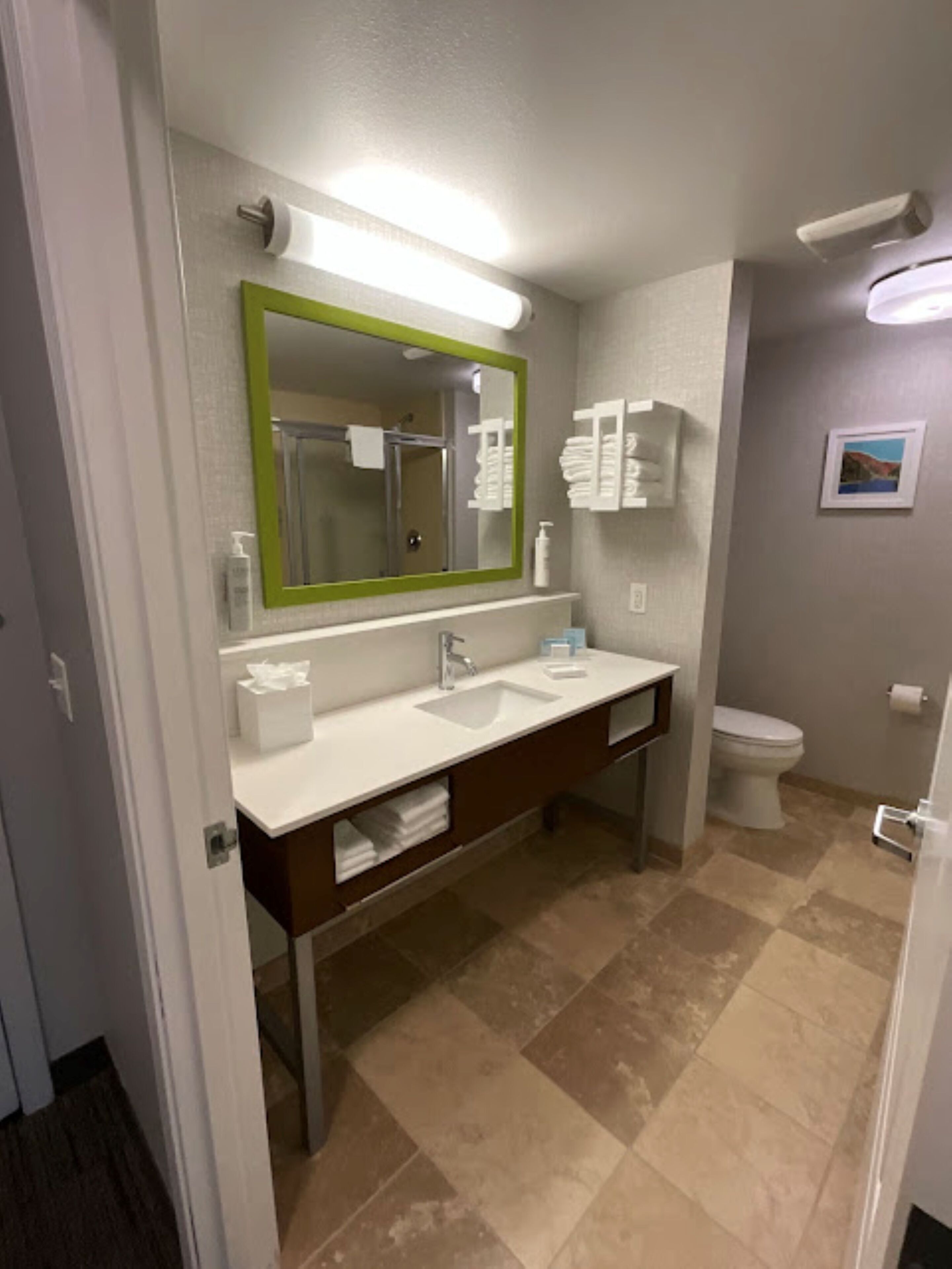 Un baño con lavamanos blanco, un espejo con marco verde, un inodoro y zona de ducha.
