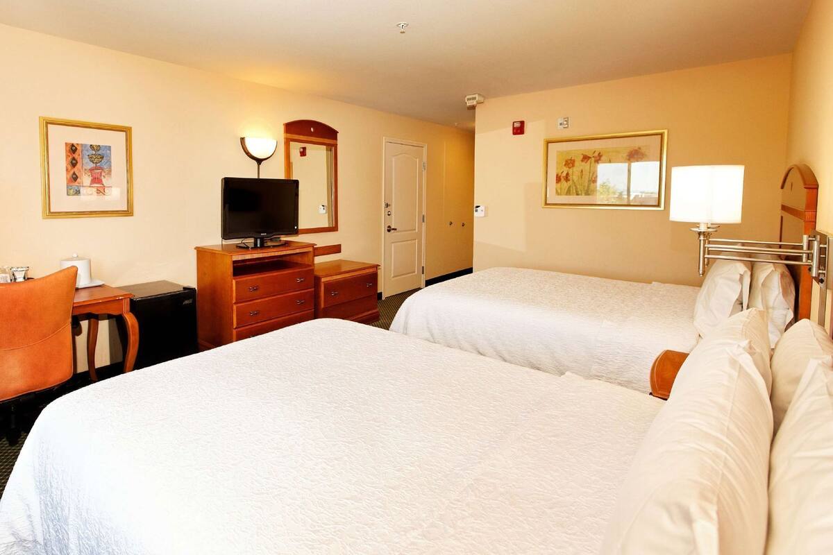 A hotel room with two beds, a desk with a television, a dresser, and artwork on the walls.